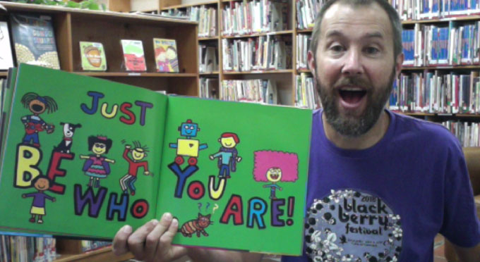 Man holding up kids book in library.