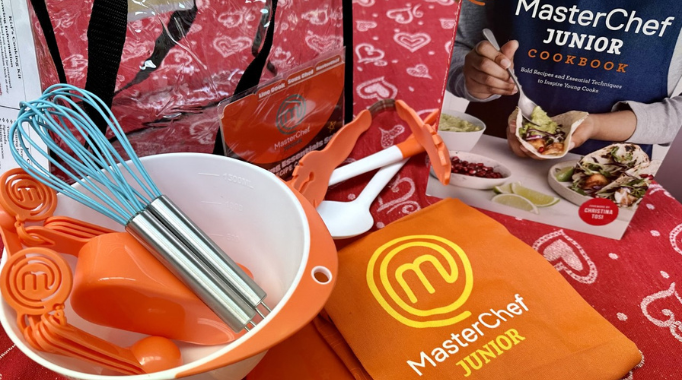 Cooking kits for kids with MasterChef Junior cookbook and apron, mixing bowl, whisk, measuring cups on a table.