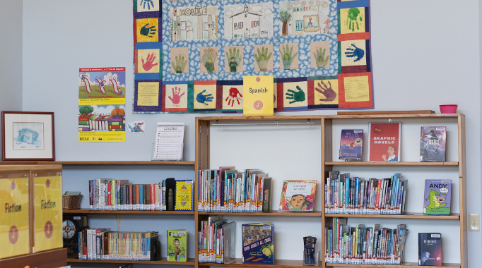 Bookshelves and books in children's library with hanging quilt.