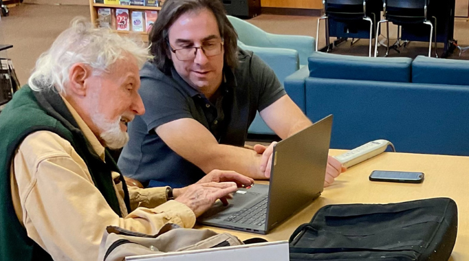 Two men sitting in front of open laptop.