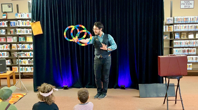 Magician on a makeshift stage area twirling rings in a show for children.