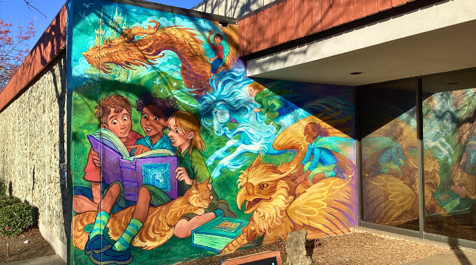 Mural depicting kids reading a book and imagining dragon, unicorn, and griffin fantasy scene, on exterior of Ukiah Library building.
