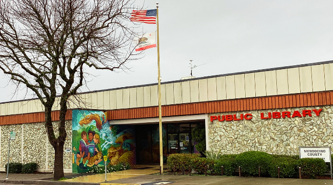 Exterior of the Ukiah Library building with flag pole and tree.