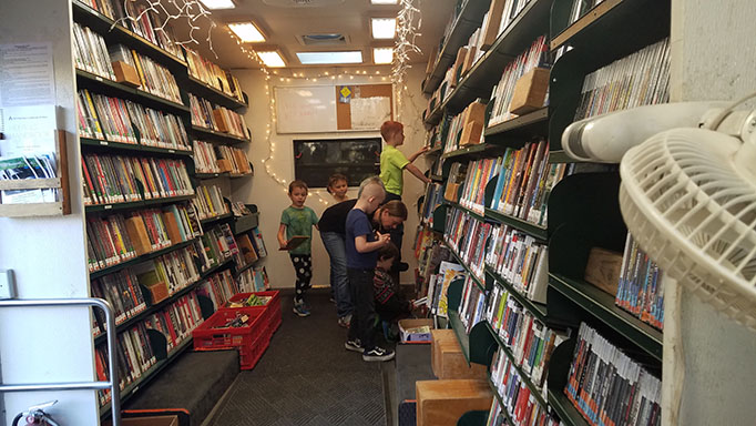 Kids standing inside the Bookmobile looking at the bookshelves.