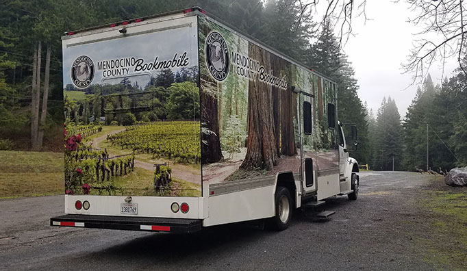 Back view of Bookmobile parked along road next to trees.