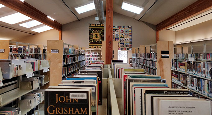 Bookshelves inside the Fort Bragg Library, with quilts on the wall.